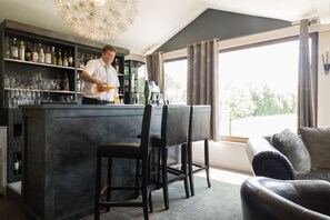 Zona de bar con un bartender, una estantería para vinos y vistas al exterior.