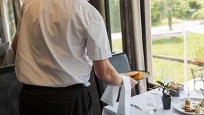 Un camarero sirve un plato en una mesa con vistas a la ventana.