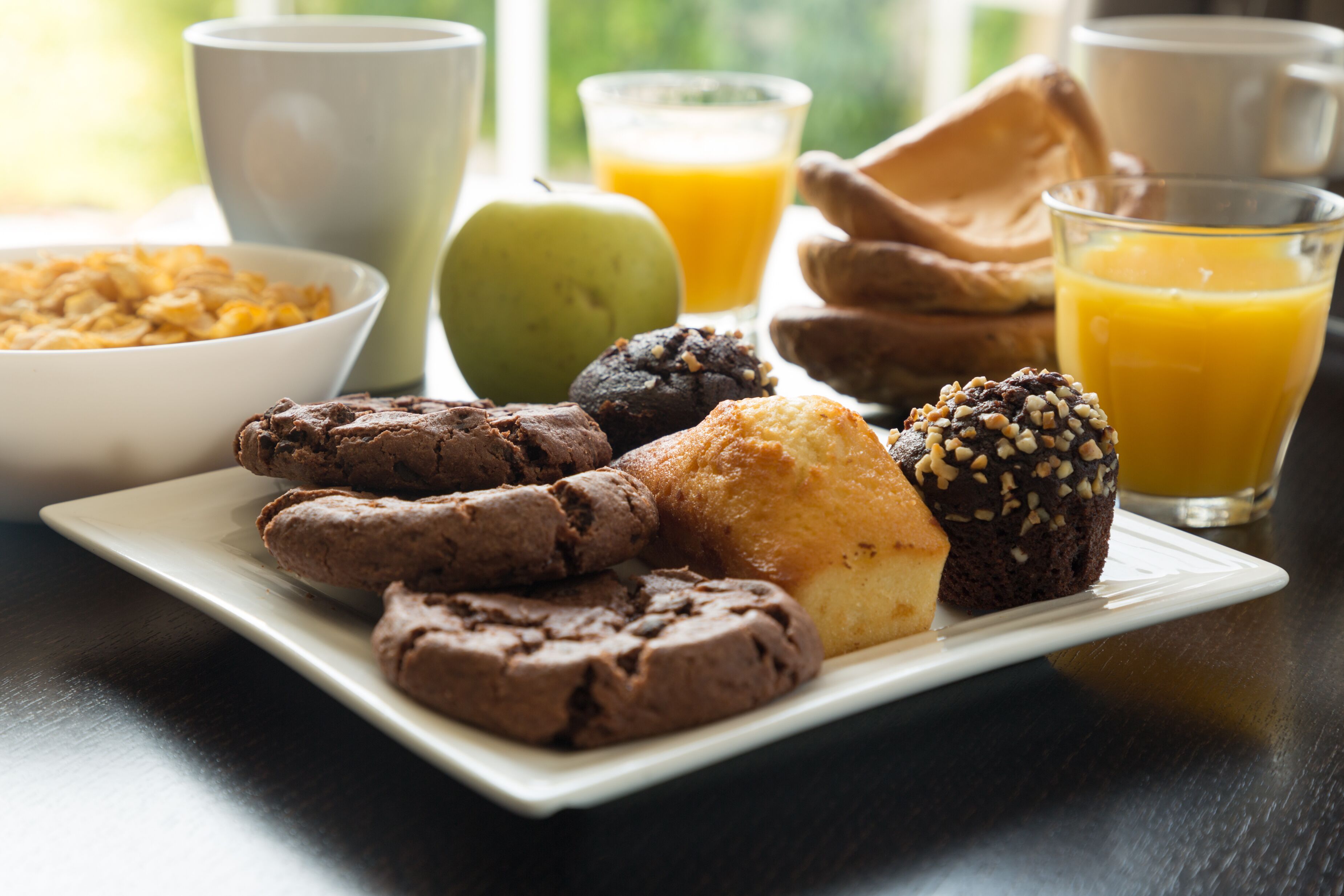 A breakfast plate with cookies, a muffin, and a glass of orange juice.
