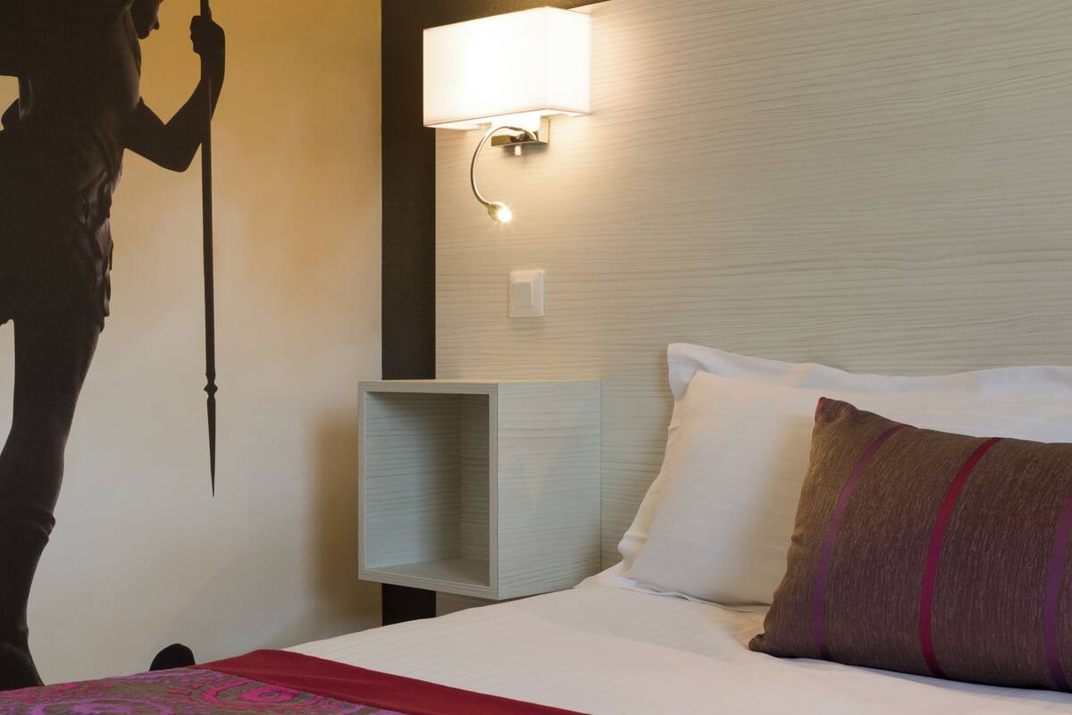 Habitació d'hotel amb un llit, una tauleta de nit, una làmpada penjada a la paret i una decoració mural.