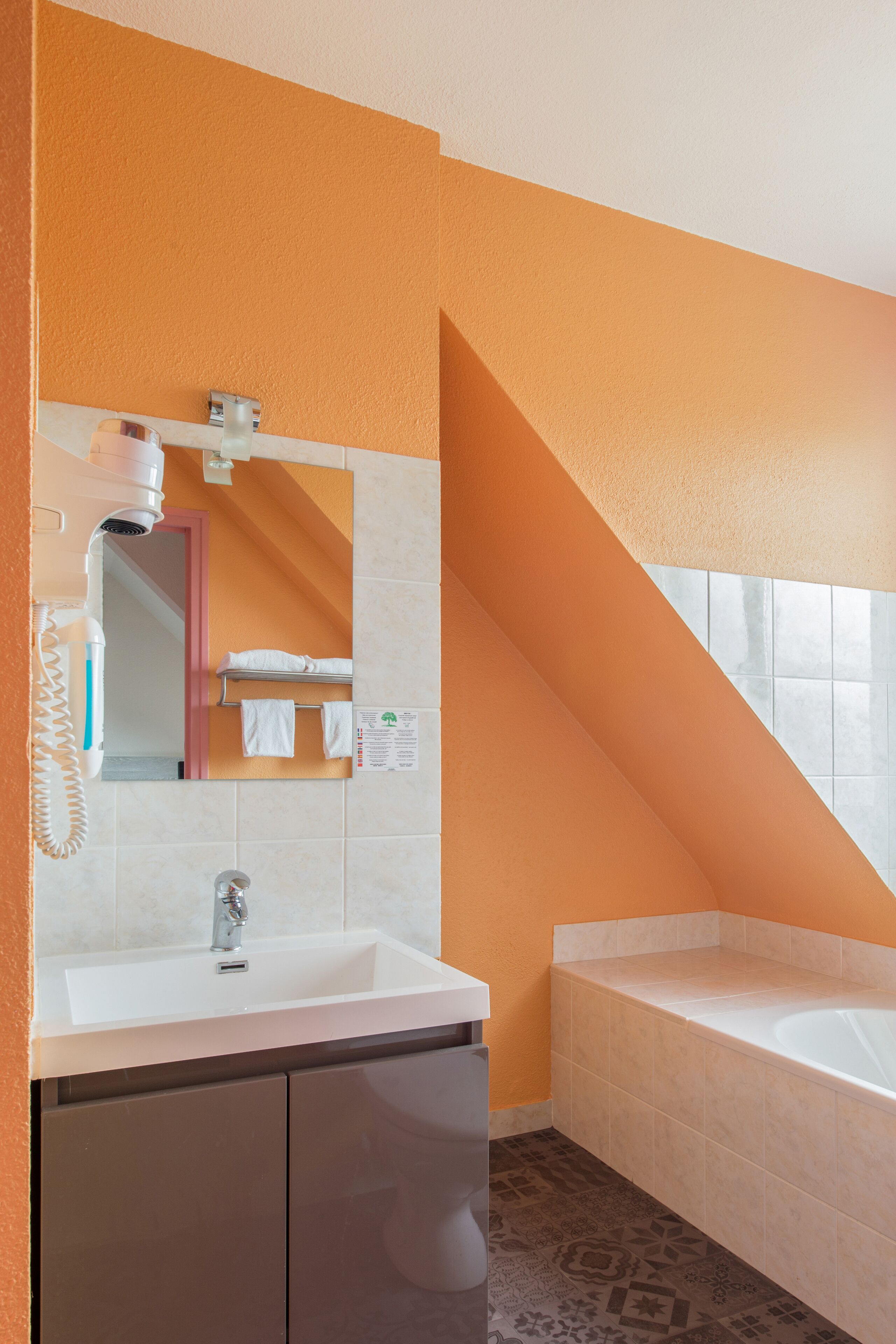 Een moderne badkamer met een witte wastafel, een spiegel, een haardroger en een bad.