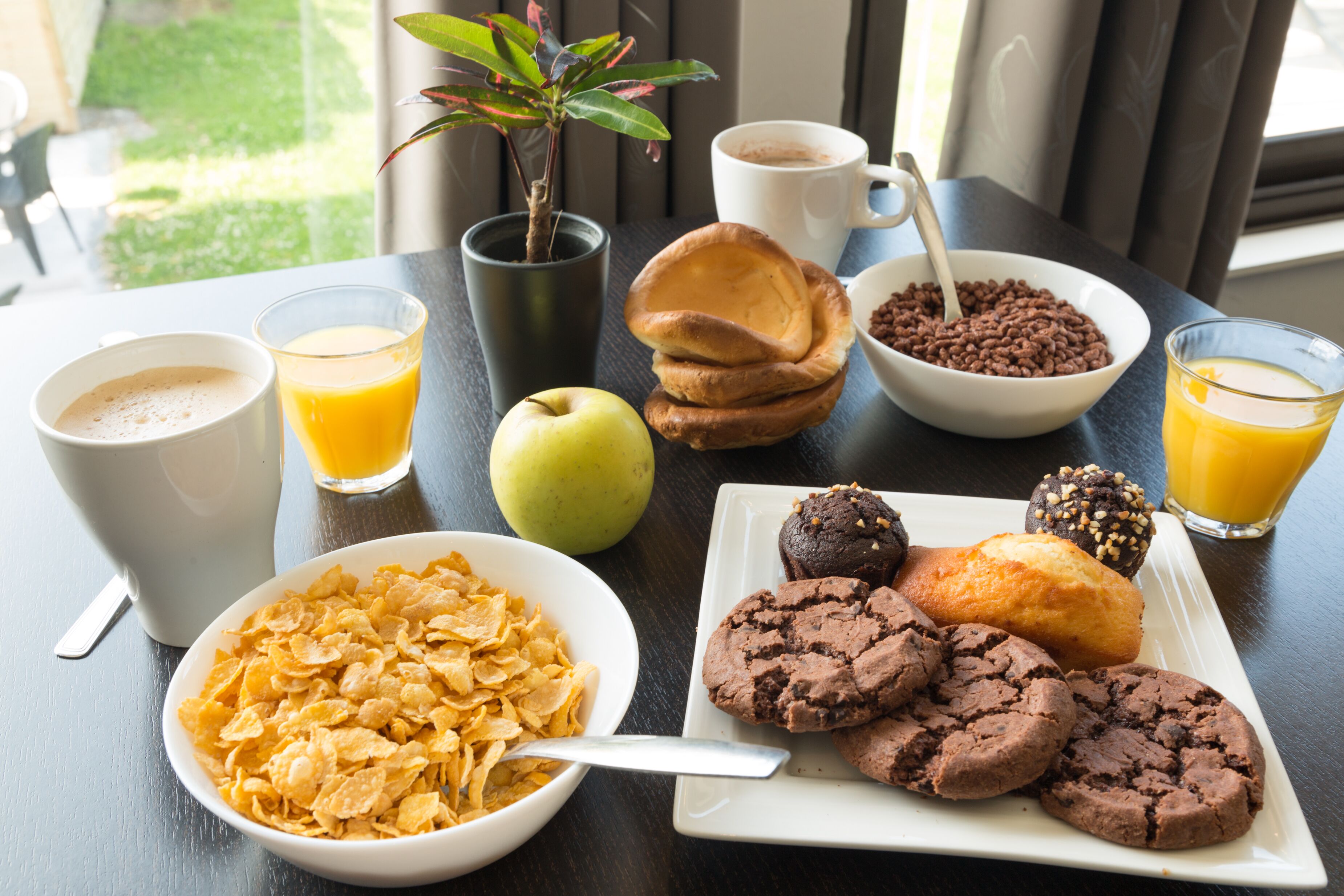 A breakfast table with cereal, coffee, juice, an apple, cookies, and pastries.