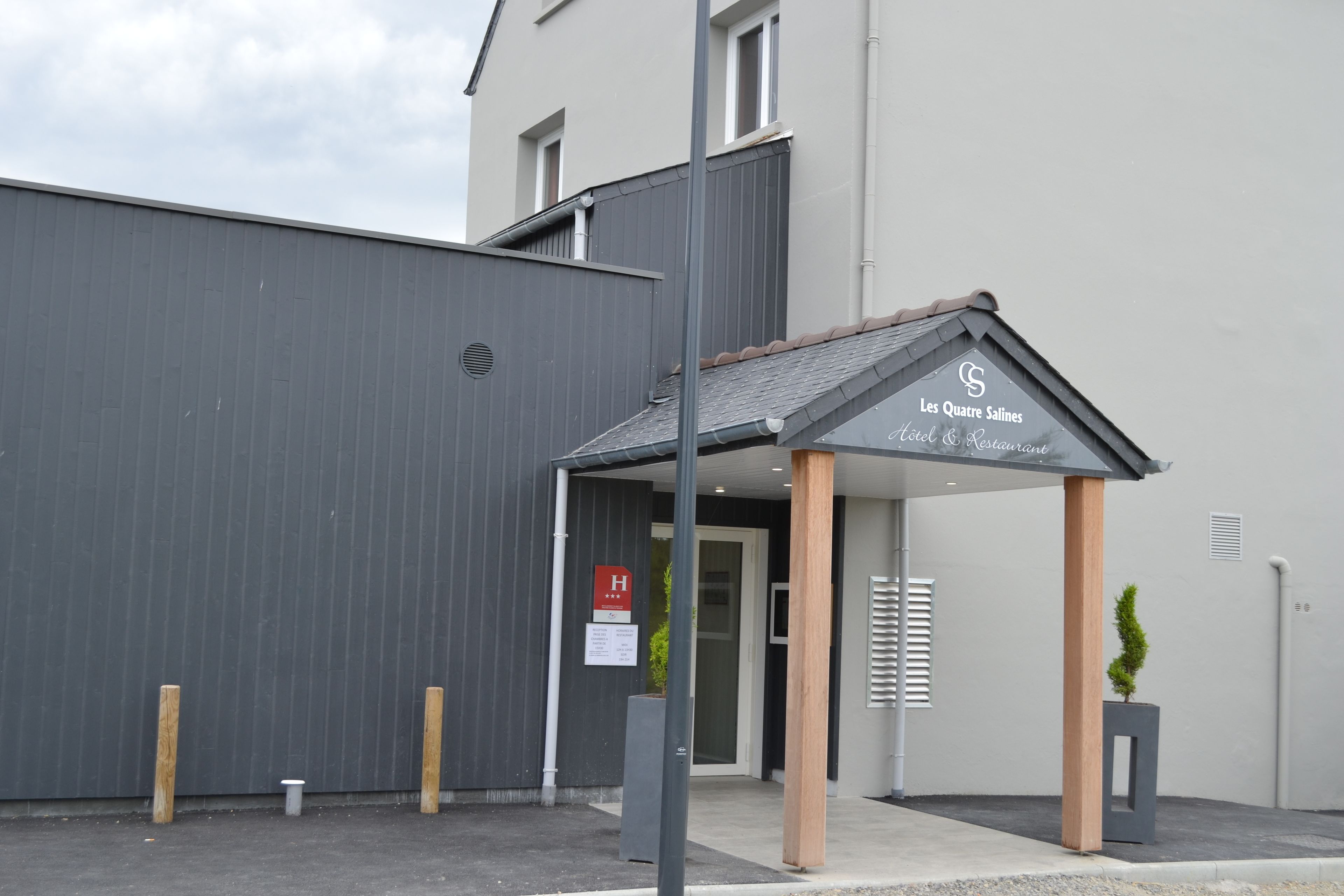 A modern hotel entrance with a grey facade, a covered entrance area, and a sign indicating it is a hotel and restaurant.