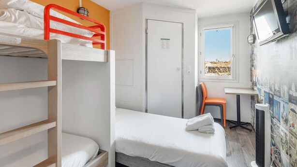 A room with a bunk bed, a single bed, a desk with a chair, a TV, and a wall with posters. - hotelF1 Lyon Bourgoin-Jallieu (L'Isle-d'Abeau)