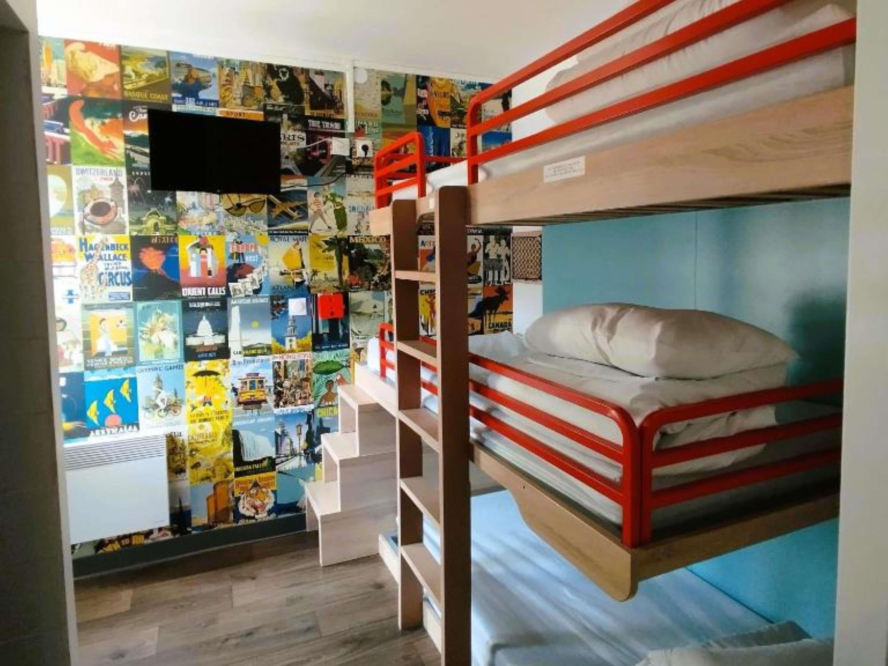 Habitación con literas, carteles en la pared, televisión y ventana.