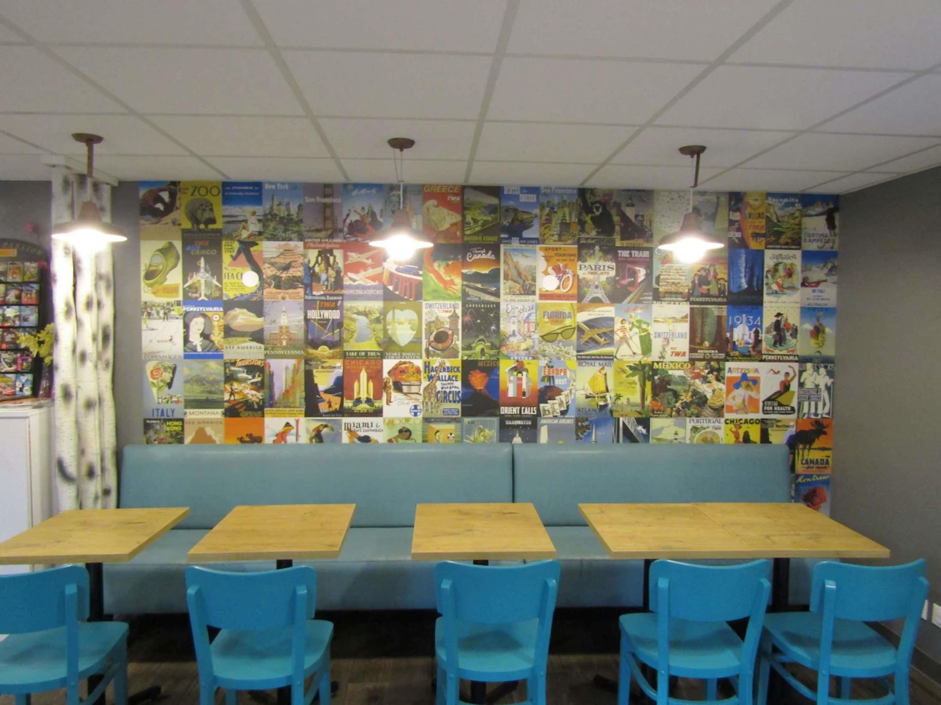 A restaurant with a wall of travel posters, blue chairs, and wooden tables.