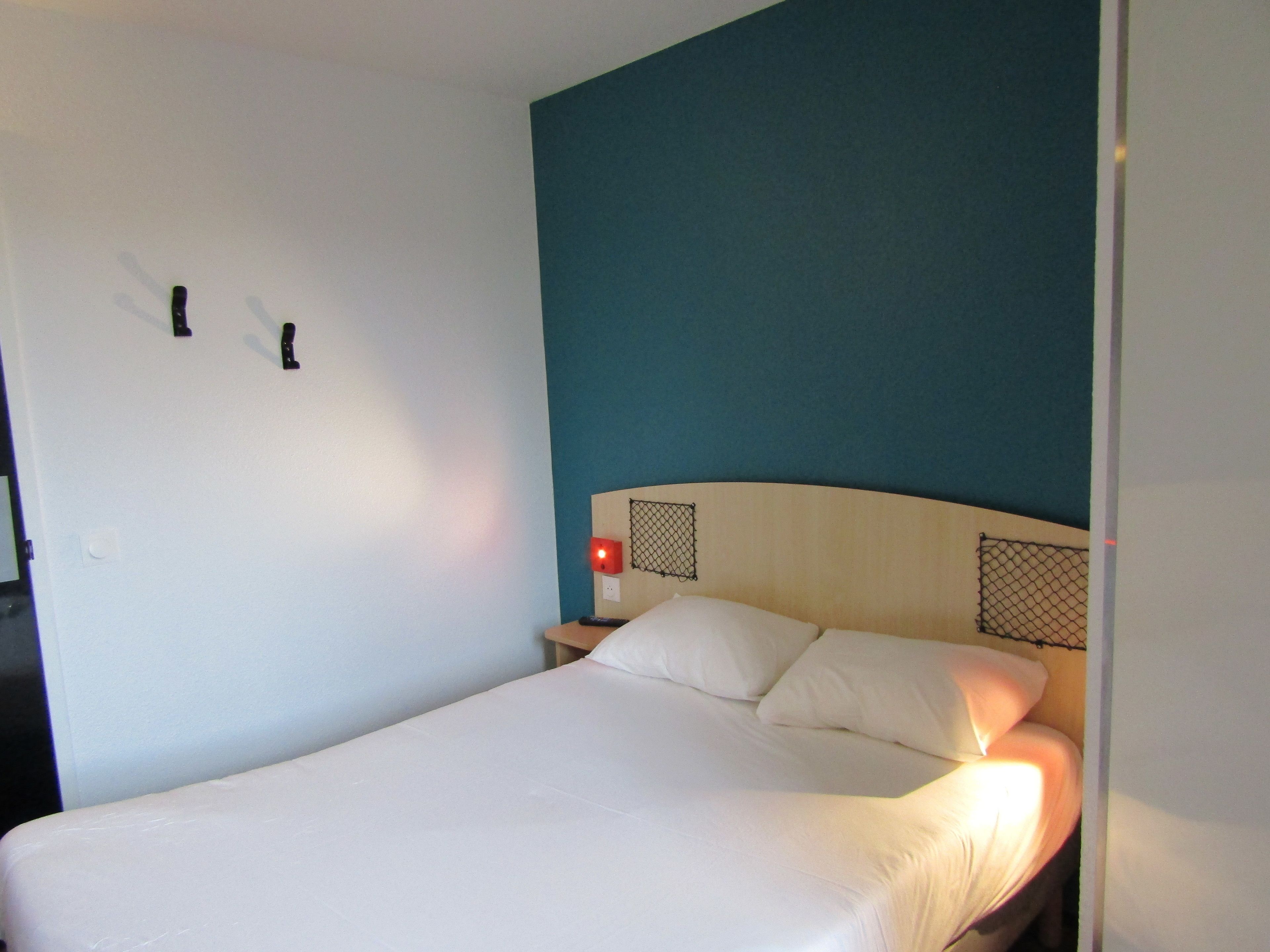 Una cama individual con ropa de cama blanca en una habitación con paredes color turquesa y cabecera de madera.