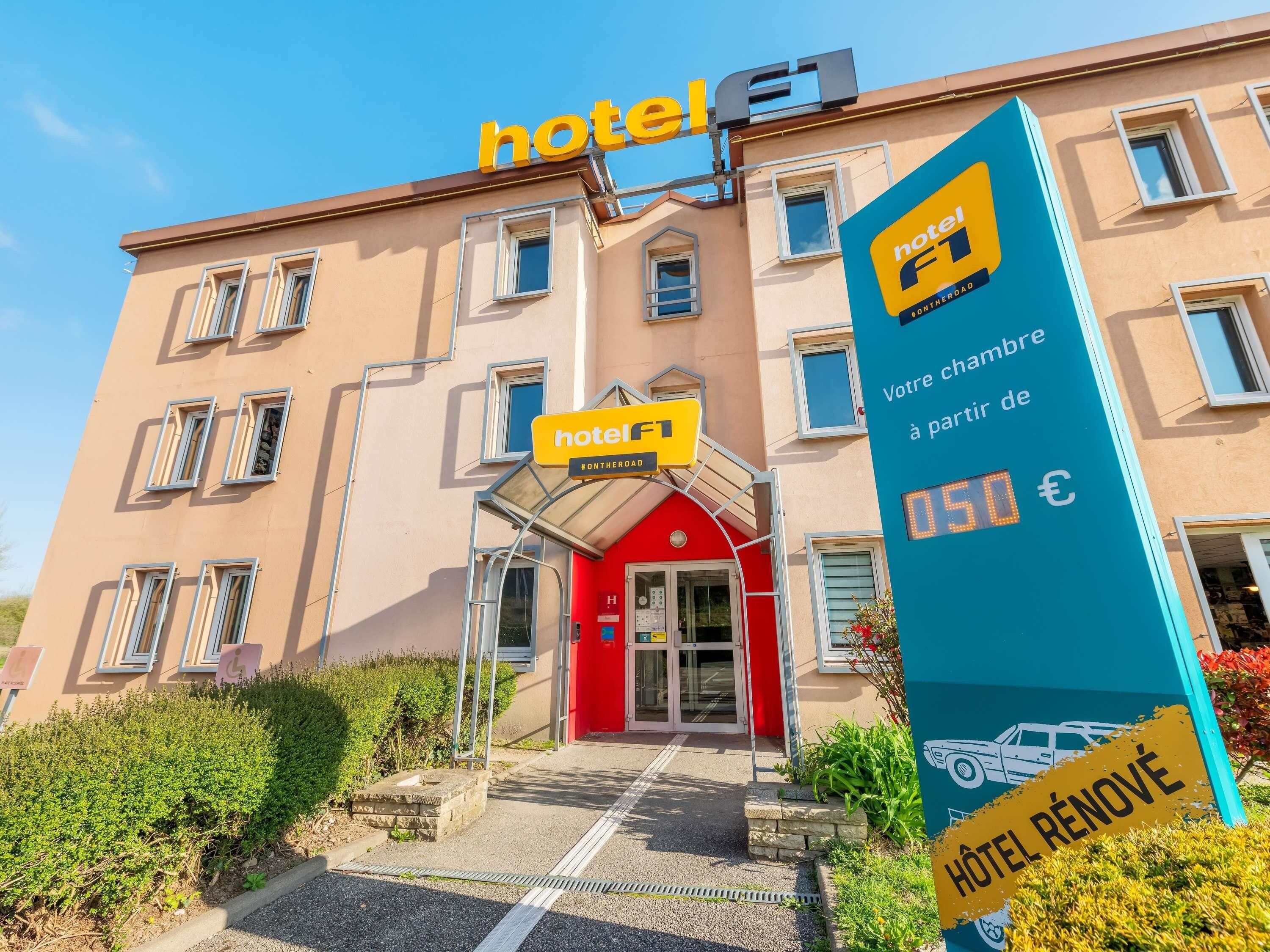 Een hotelgebouw met een rode ingang, een geel bord waarop 'hotel F1' staat en een digitaal scherm dat '050 €' toont.