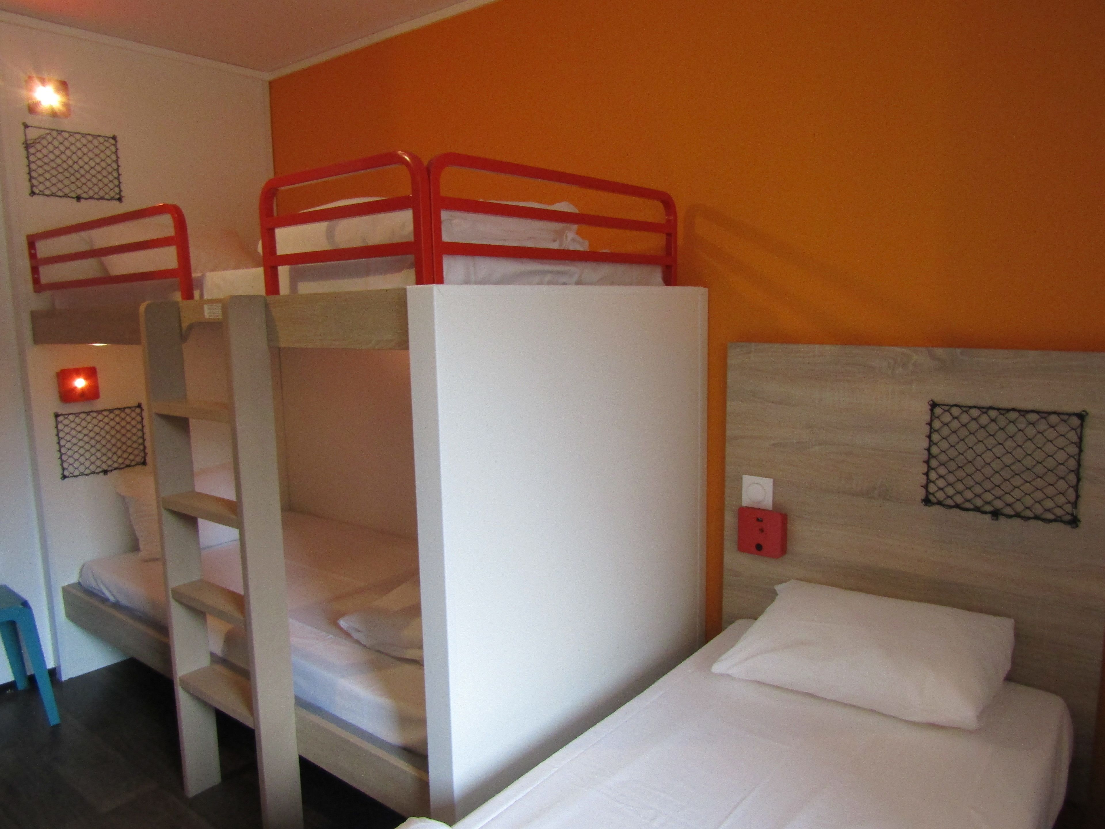 A bunk bed room with a wooden headboard, a single bed with white bedding, and a red ladder.