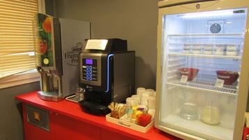 A self-service coffee station with a digital coffee machine, a refrigerator stocked with beverages, and a display of various coffee pods and accessories.