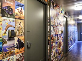 Un pasillo con carteles de viajes en las paredes, una puerta y suelo de madera.
