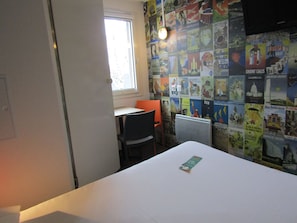 Una habitación con una cama, un escritorio, una silla y una pared decorada con carteles de viajes.
