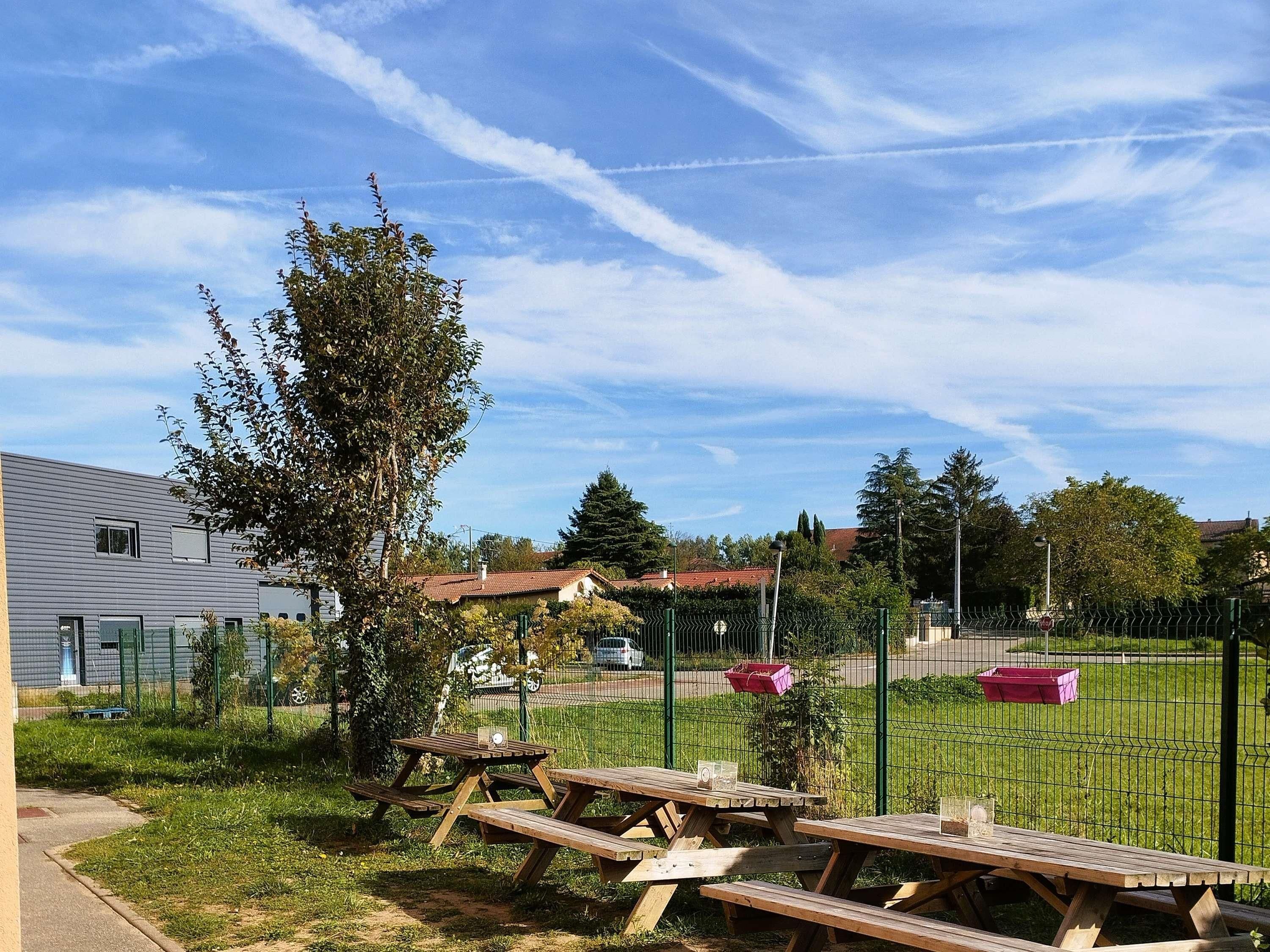 Un espace de pique-nique avec des bancs et une aire de jeux clôturée, situé dans un quartier résidentiel.