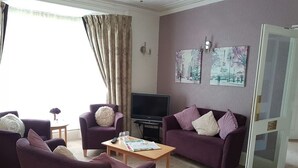 A living room with purple sofas, a coffee table, a TV, and artwork on the wall.