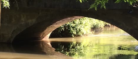 A stone bridge over a calm river with lush greenery on both sides.