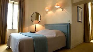 A neatly made bed with a blue headboard, a bedside lamp, and a wall-mounted mirror.