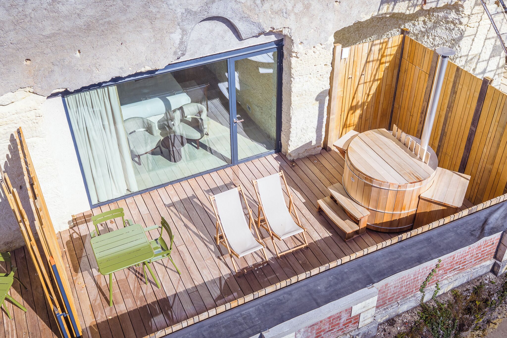 Eine Holzdar Terrasse mit Glastür zu einem Raum, eine Holzsauna und Sitzgelegenheiten im Freien.