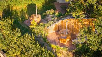 Une terrasse en bois dotée d’un jacuzzi et d’un espace salon, le tout entouré d’une végétation luxuriante.