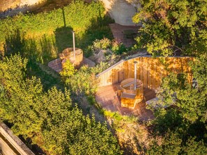 Terraza de madera con jacuzzi y zona de estar rodeada de exuberante follaje.