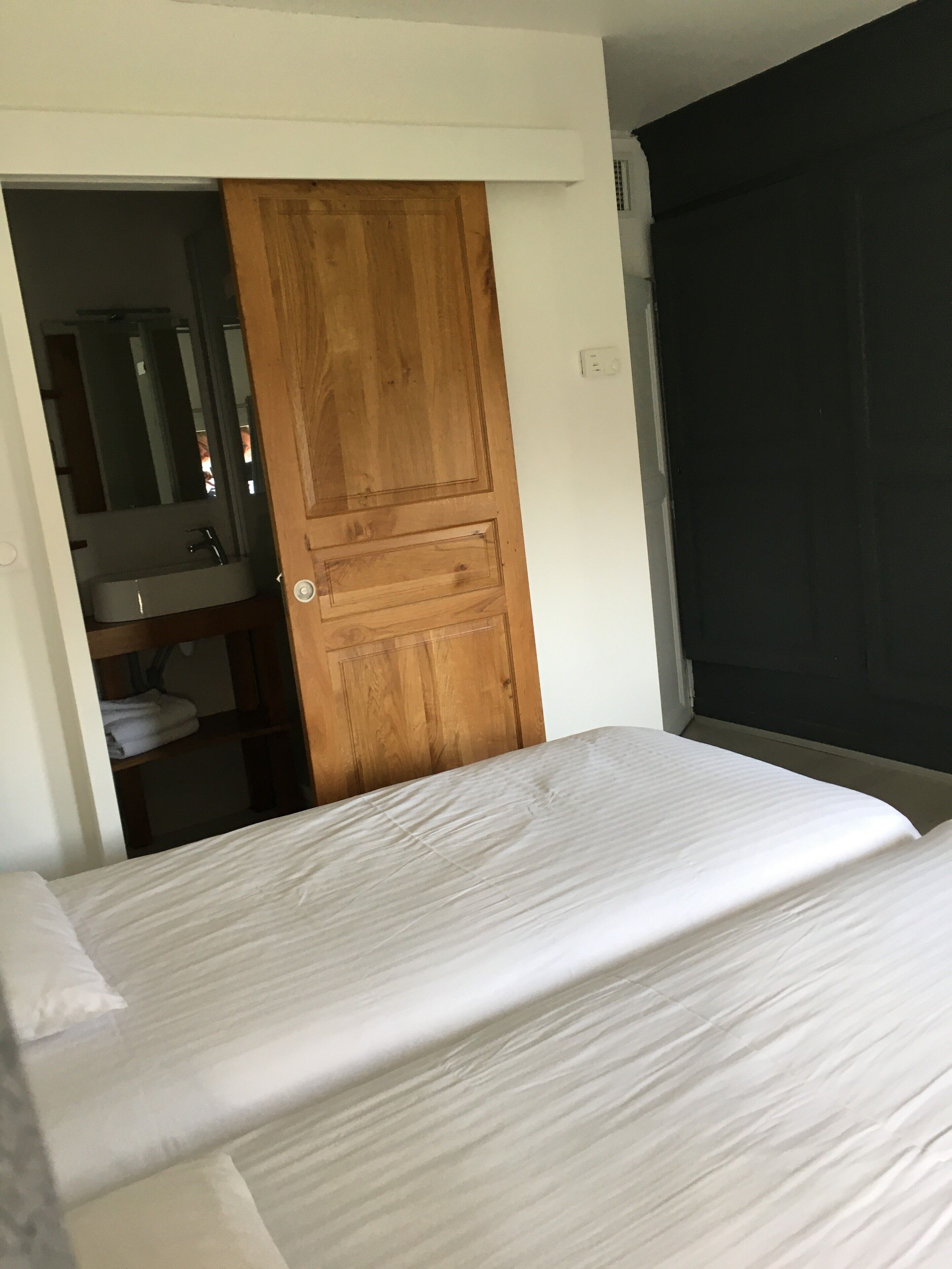 Una camera da letto con un letto, una porta in legno, un bagno con lavandino e specchio, e una finestra con persiana.