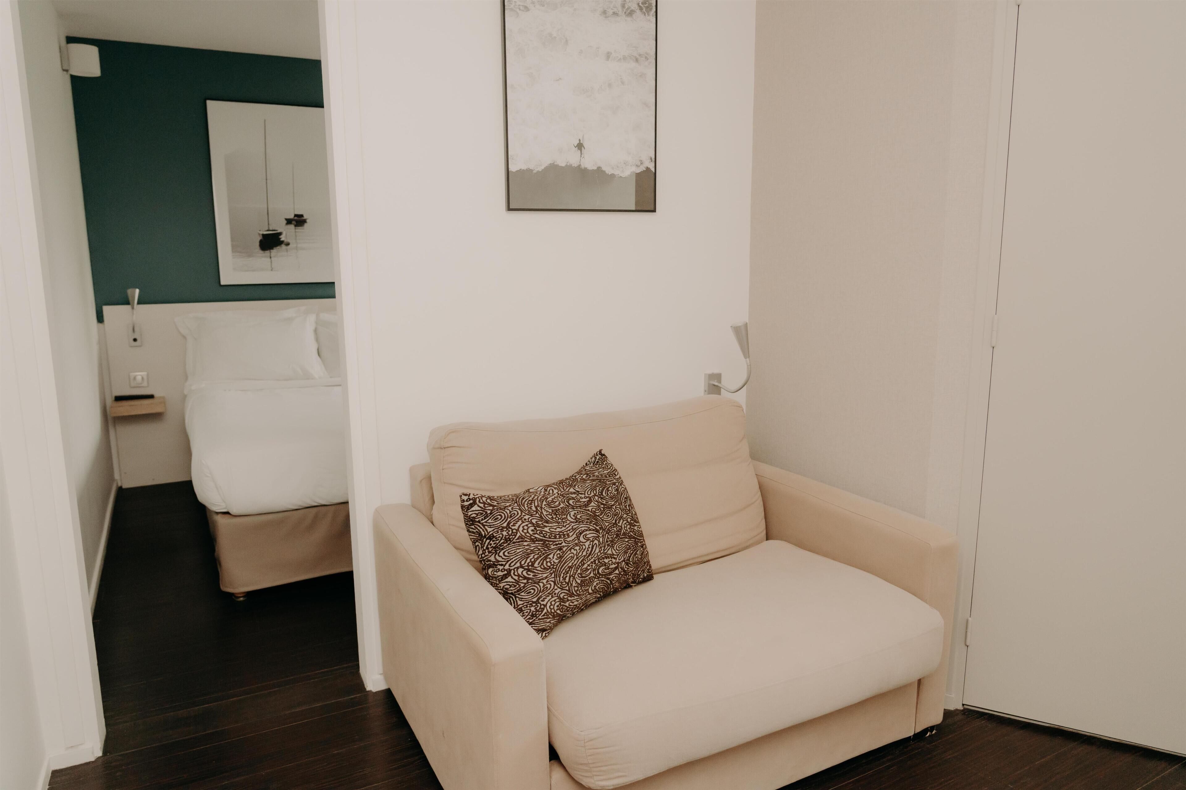 A room with a beige sofa, a patterned pillow, a white wall, and a door.