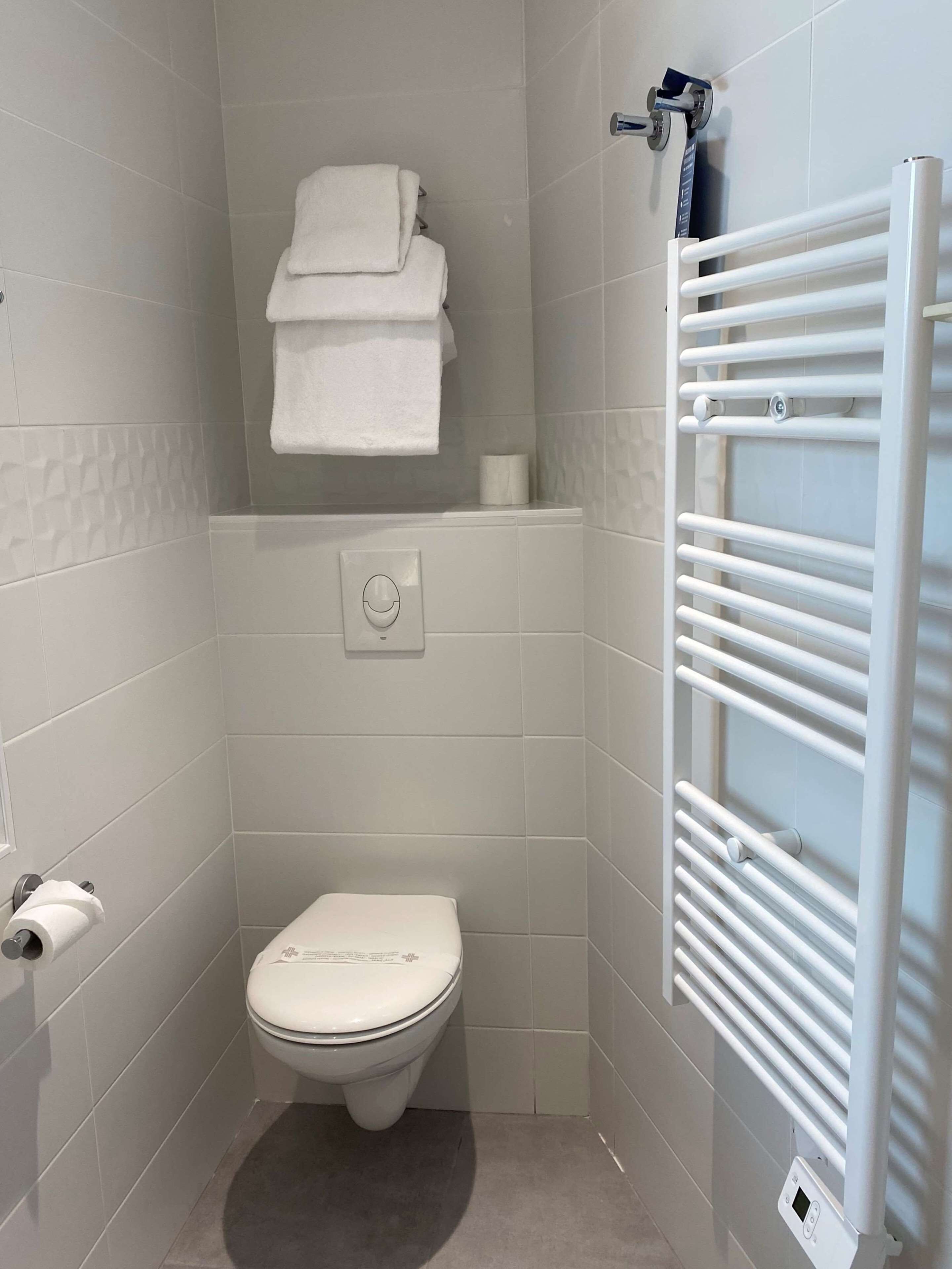 Un baño pequeño y moderno con inodoro, toallero y dispensador de papel higiénico de pared.