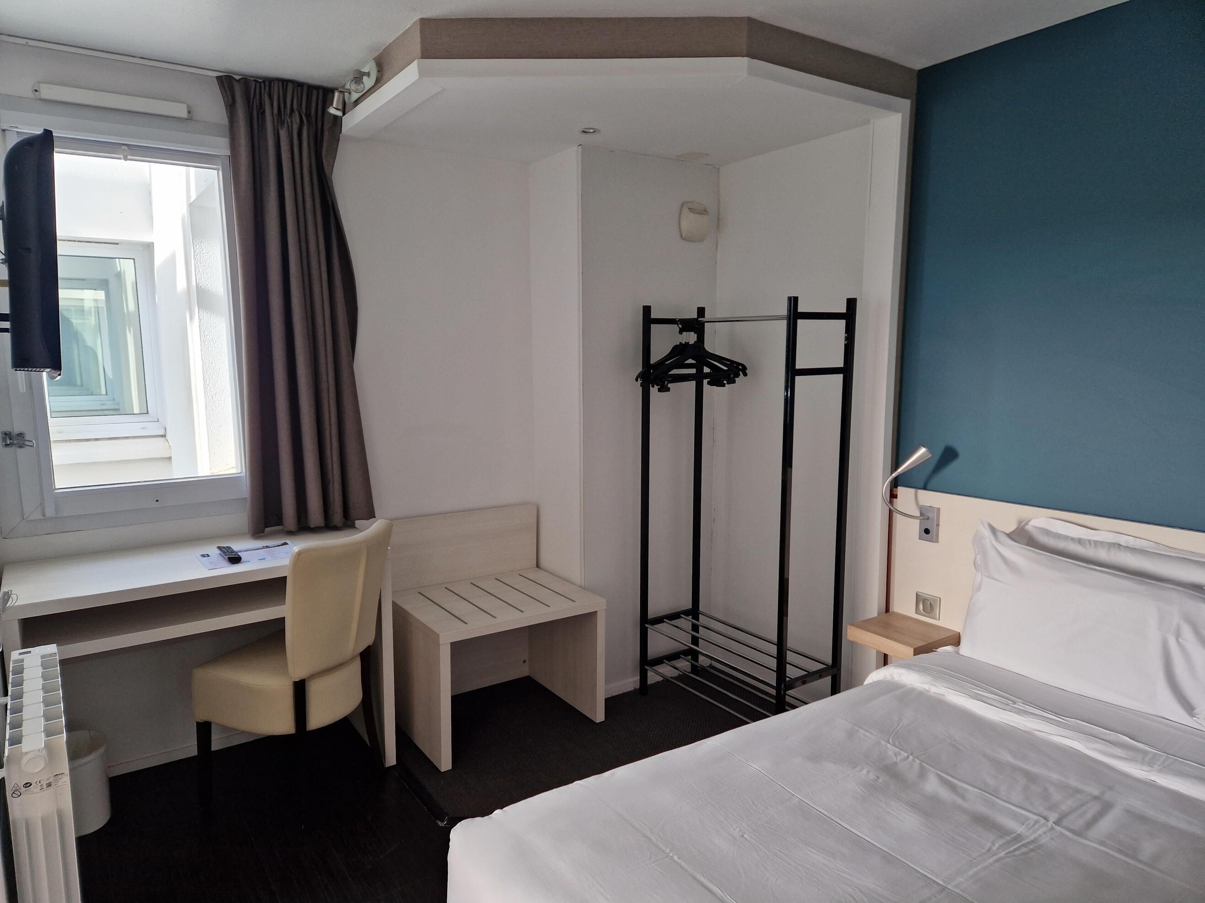 A hotel room with a bed, desk, chair, and a coat rack.