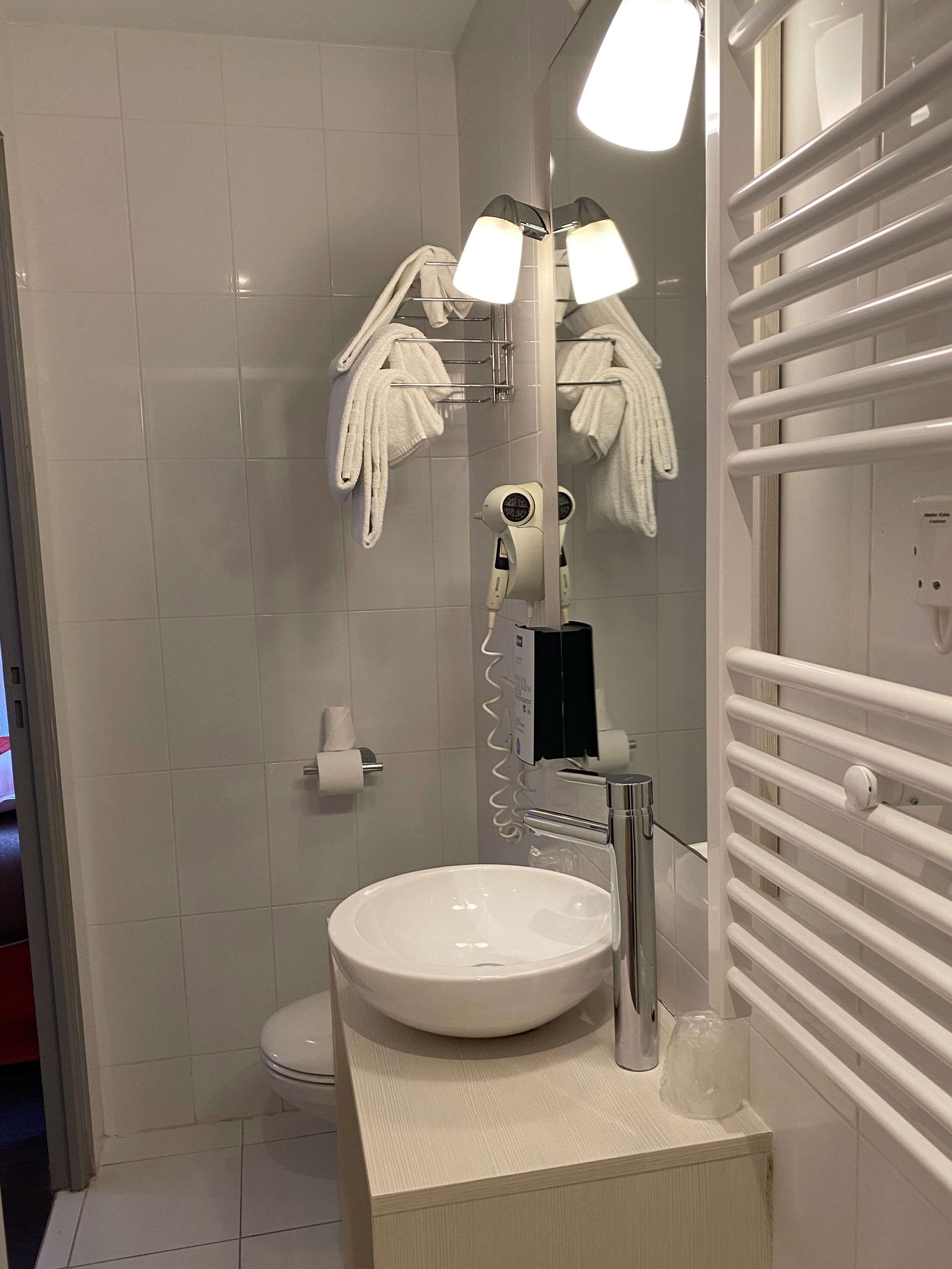 A modern bathroom with a white sink, a mirror, a towel rack, a hairdryer, and a toilet.
