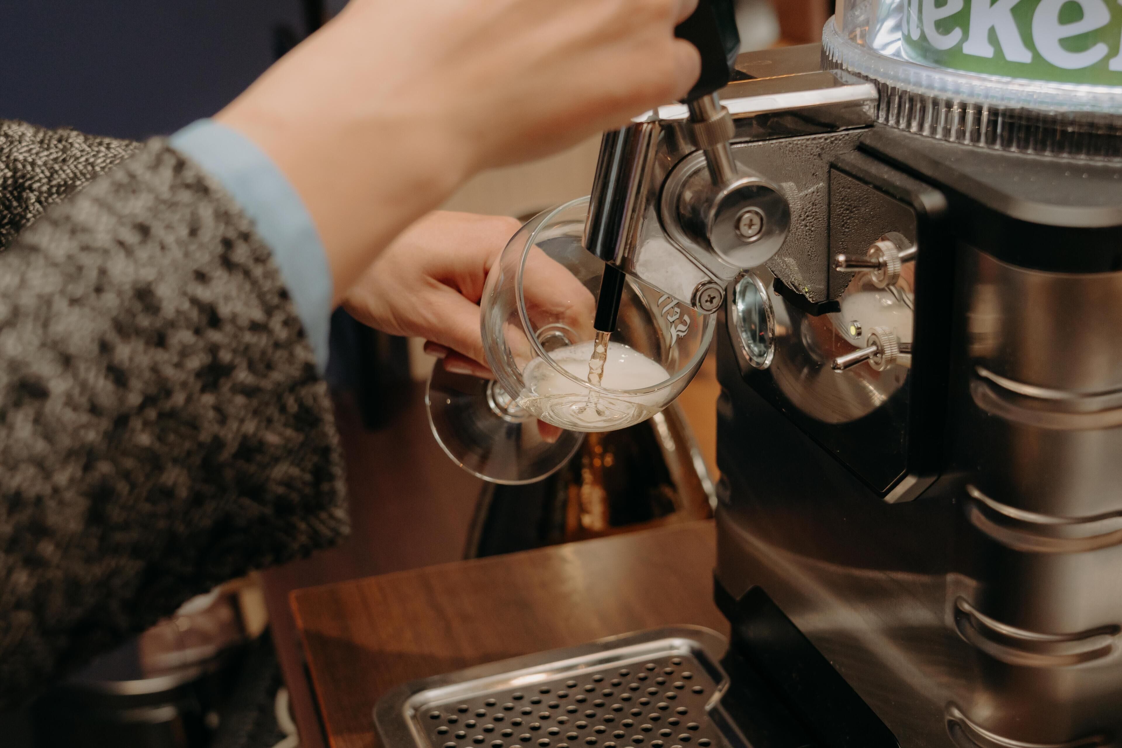 Una persona usando una máquina de café, con un recipiente de vidrio transparente y una bandeja metálica para recoger las gotas.