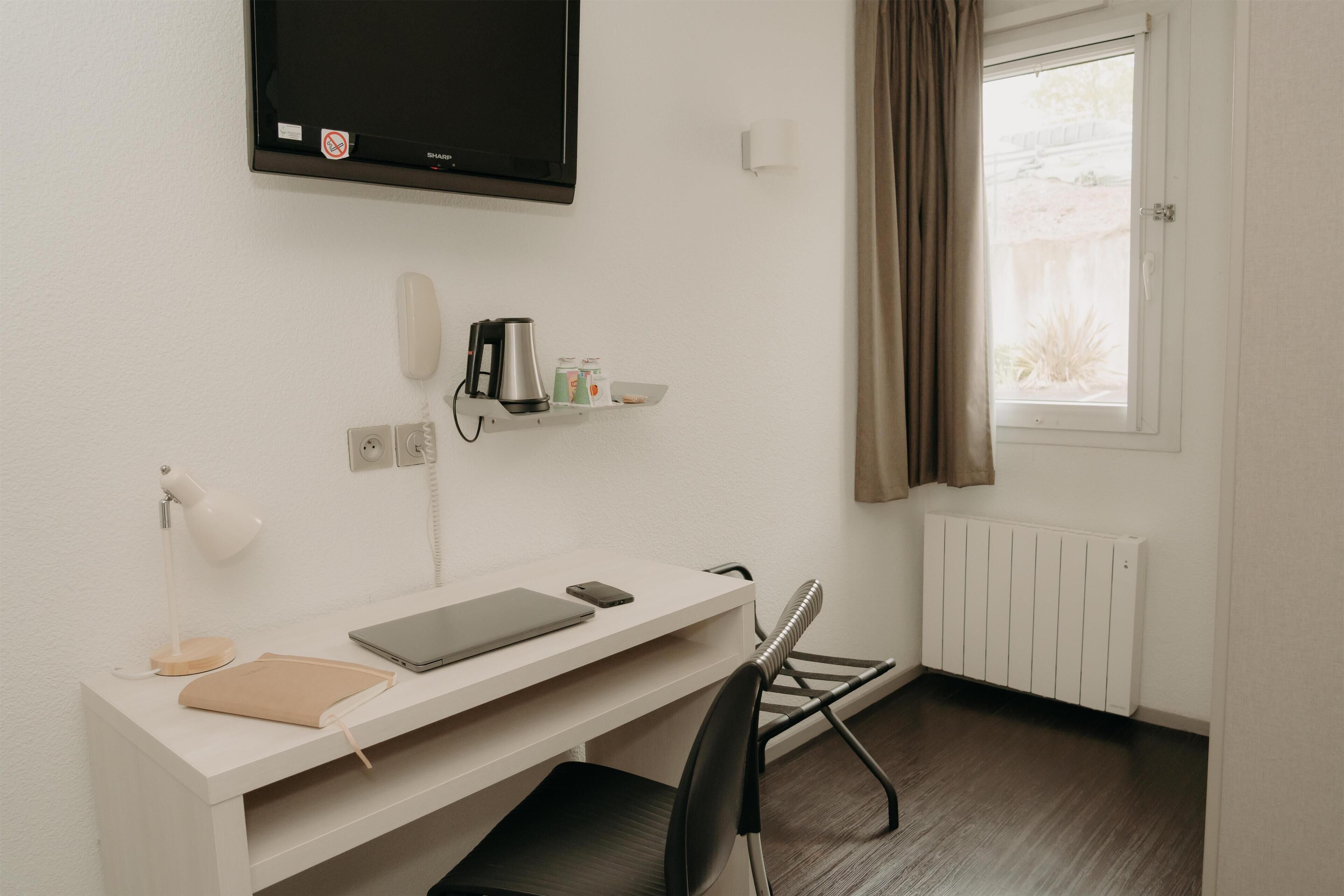 Une chambre d’hôtel équipée d’un bureau, d’une chaise, d’une télévision, d’une machine à café et d’une fenêtre avec des rideaux.