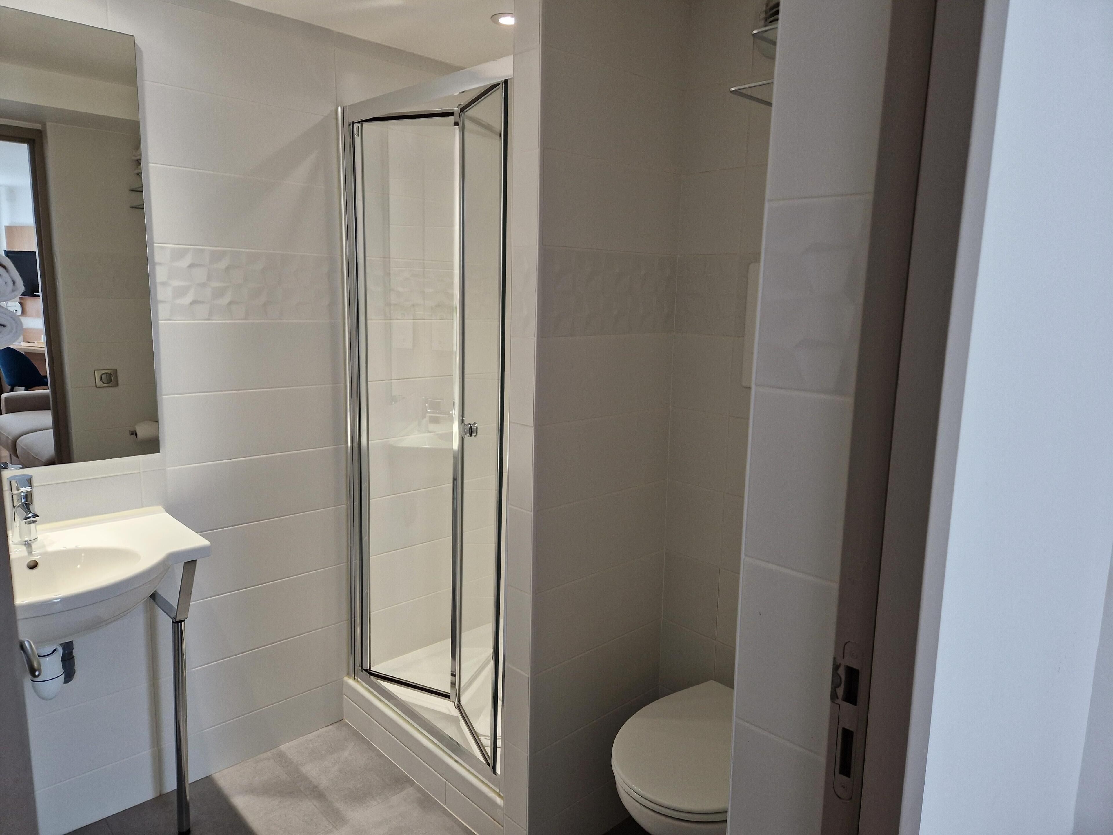 Et badeværelse med brusekabine i glas, vask og toilet.