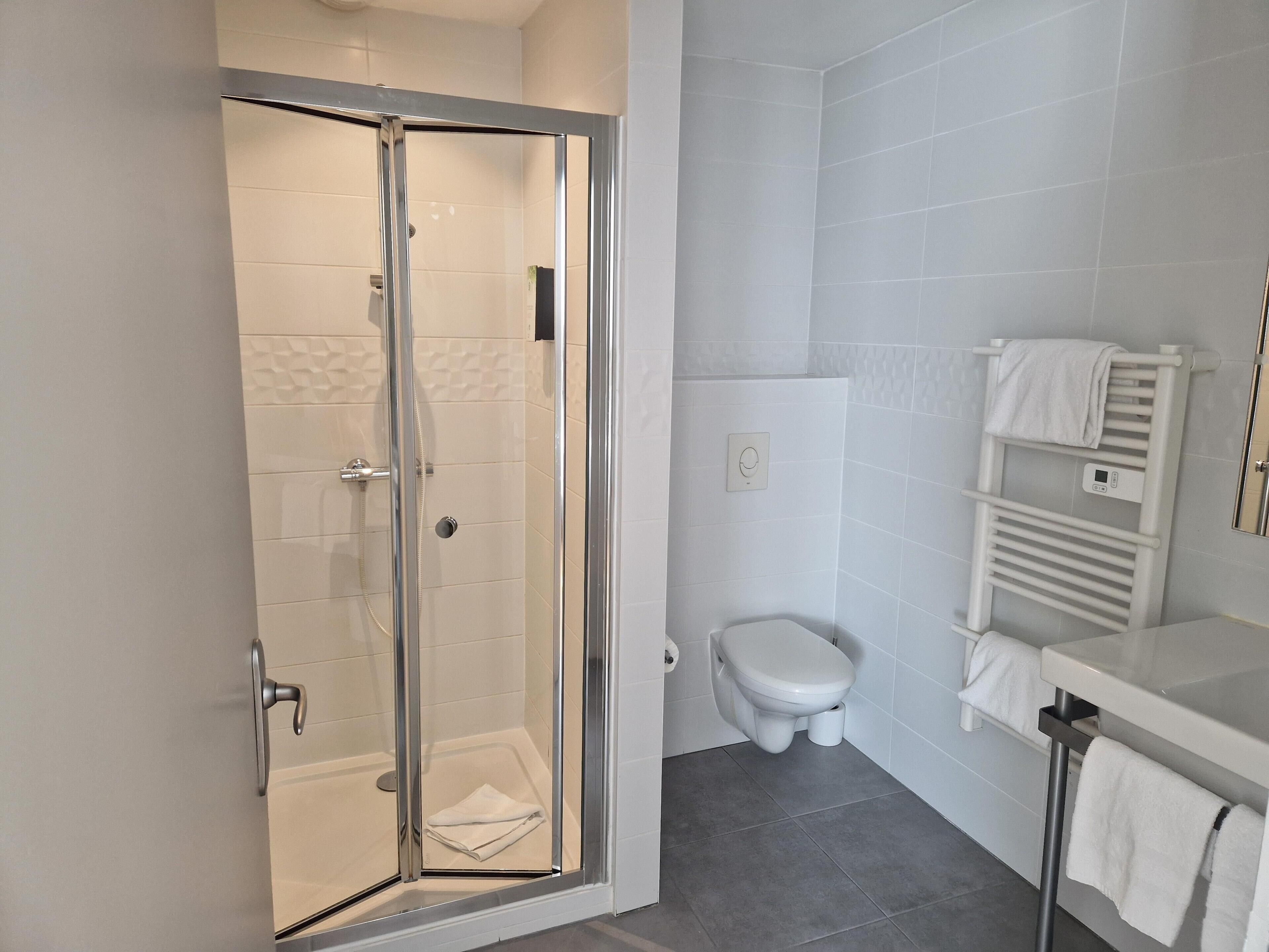 Une salle de bain moderne avec une douche à parois de verre, des toilettes et un lavabo blanc doté d’un porte-serviettes.