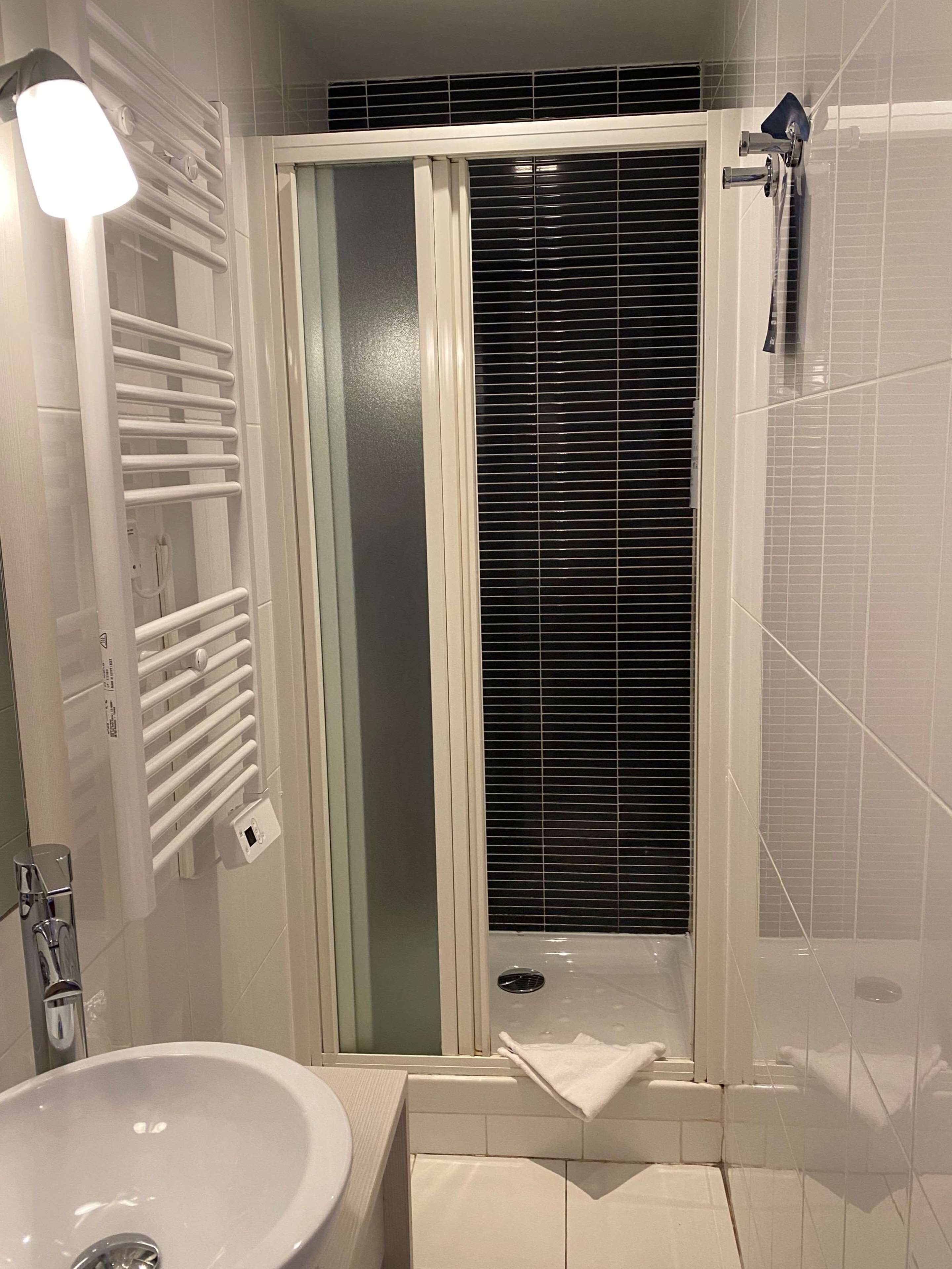 A bathroom with a shower, a sink, and a towel rack.