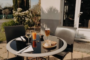 A round table with a glass of white wine, a glass of orange juice, a glass of beer, a plate with bread and a jar of spread, and a napkin. - Hôtel Kyriad Quimper Sud (Quimper)