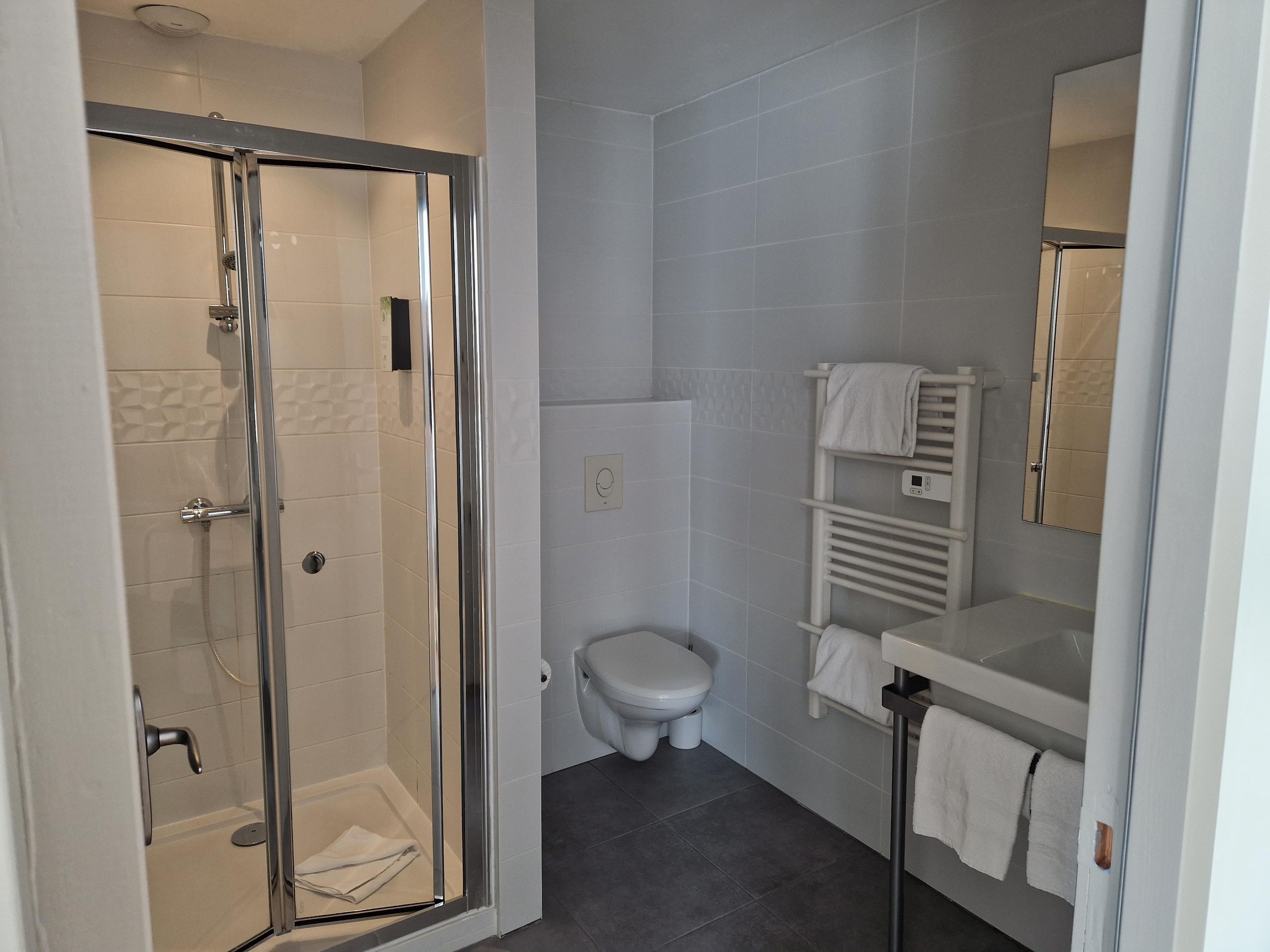 A modern bathroom with a glass-enclosed shower, a toilet, and a built-in towel rack.