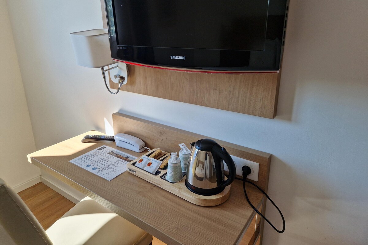 A hotel room with a wooden desk, a television, a kettle, a phone, and a cup of tea.