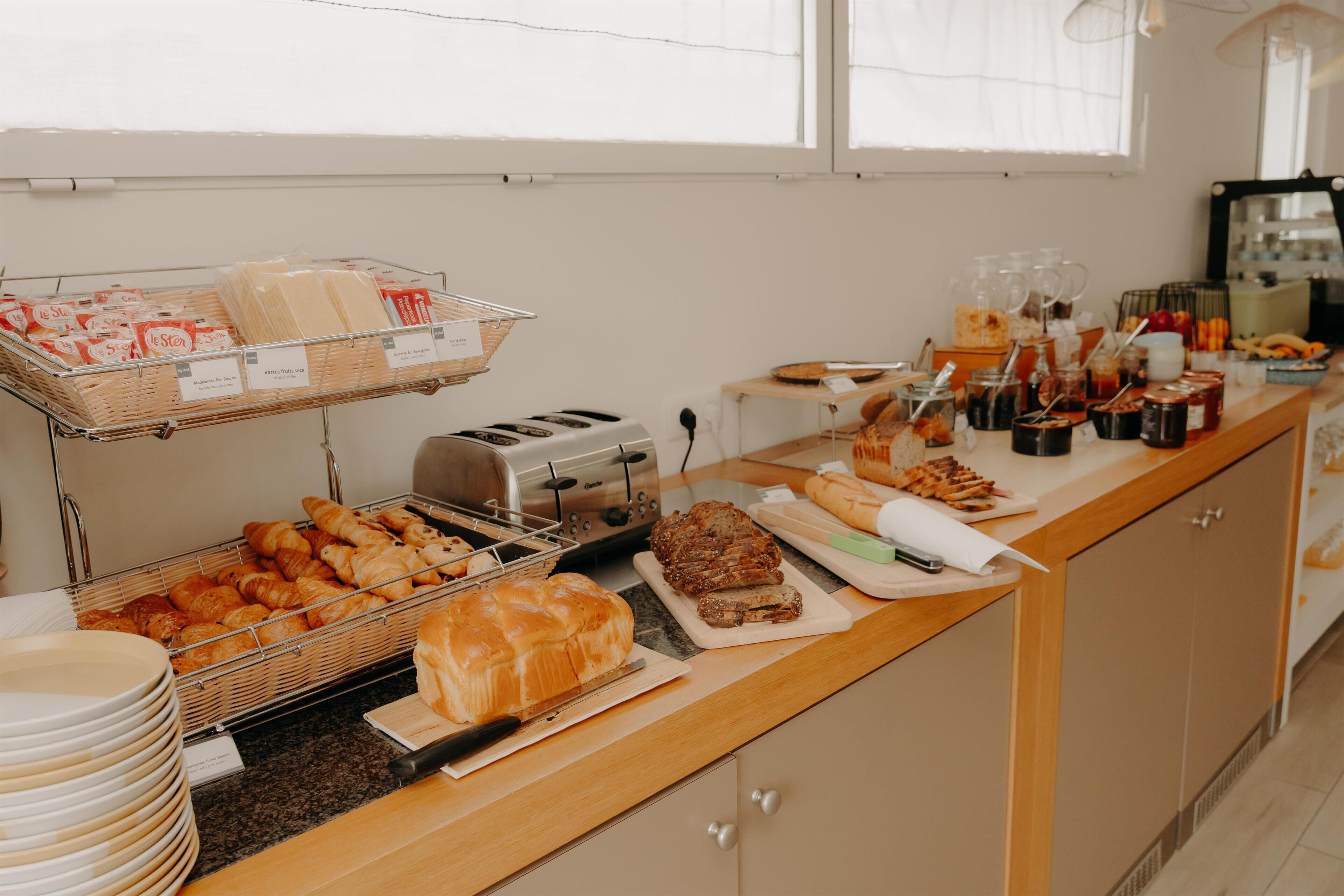A buffet setup with bread, pastries, and a variety of condiments.