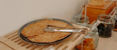 A tray of crepes on a wooden stand with tongs, a jar of orange slices, and a jar of blackberries.