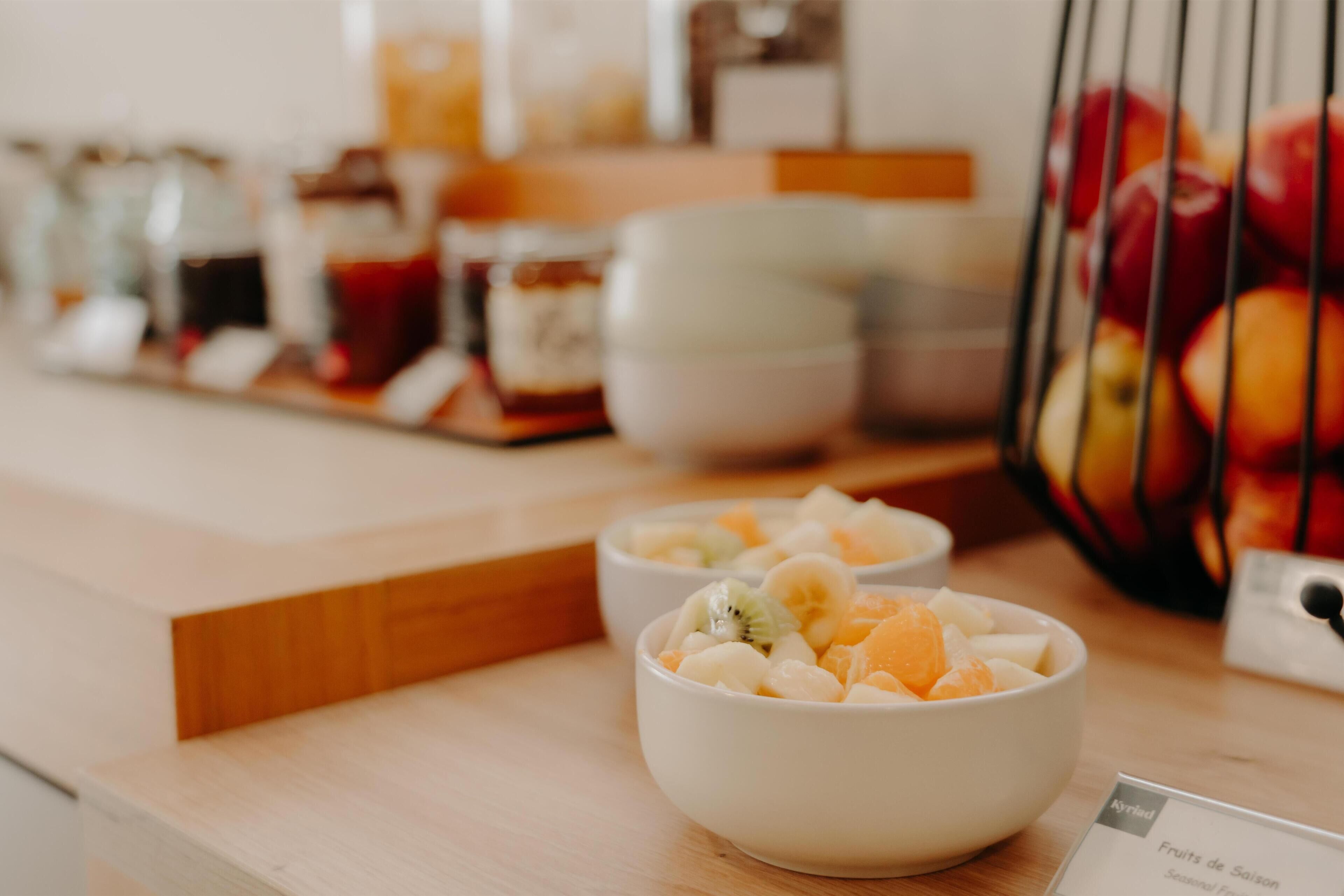 A breakfast buffet with bowls of fruit salad, a fruit basket, and a menu sign.