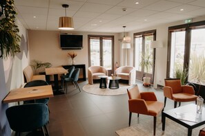 A modern hotel lobby with seating, a TV, and large windows. - Hôtel Kyriad Quimper Sud (Quimper)