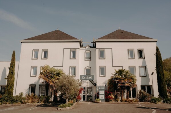 A symmetrical building with a central entrance, two symmetrical wings, and a sign indicating it is a restaurant. - Hôtel Kyriad Quimper Sud (Quimper)