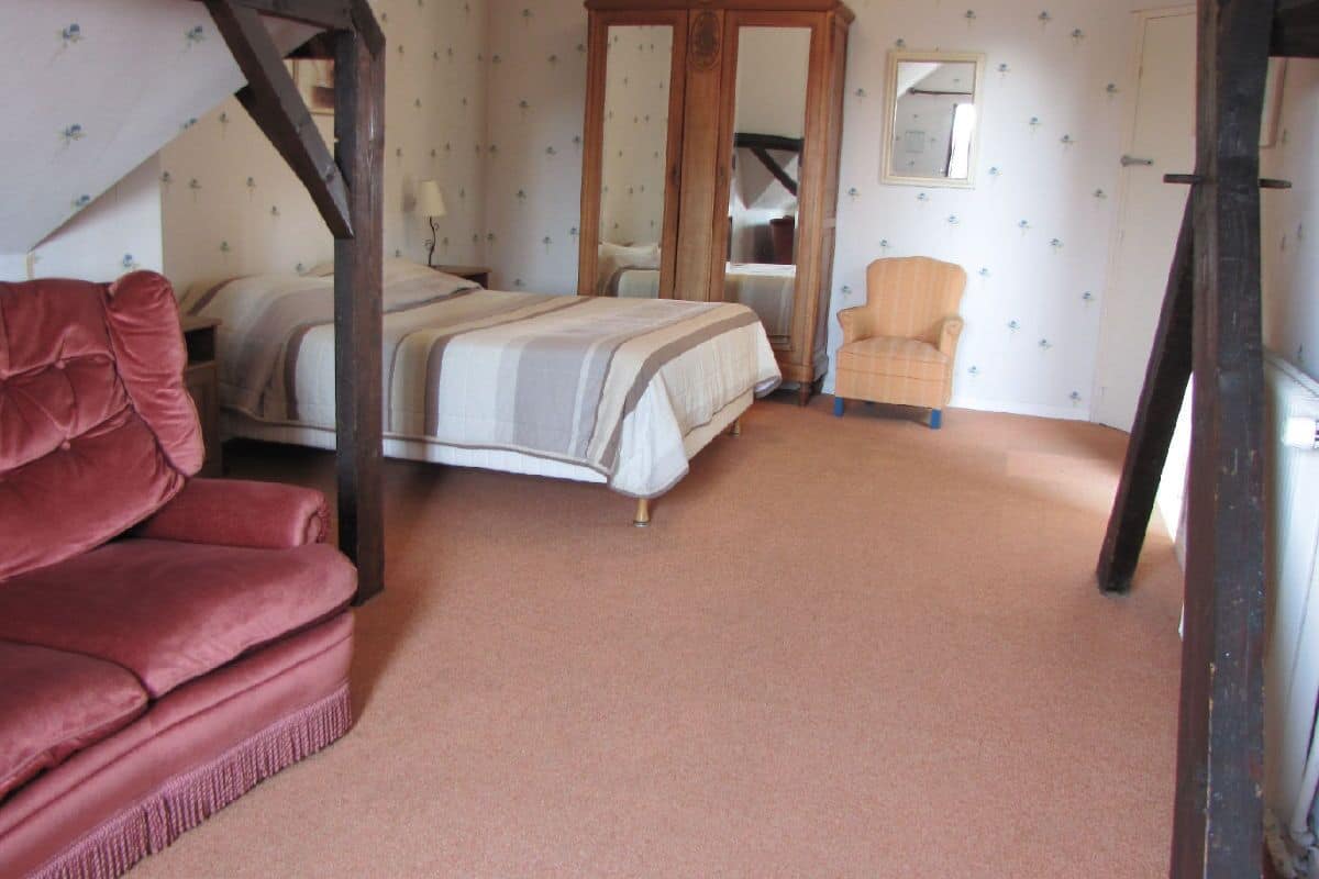 A bedroom with a bed, a red sofa, a wooden wardrobe, and a mirror.