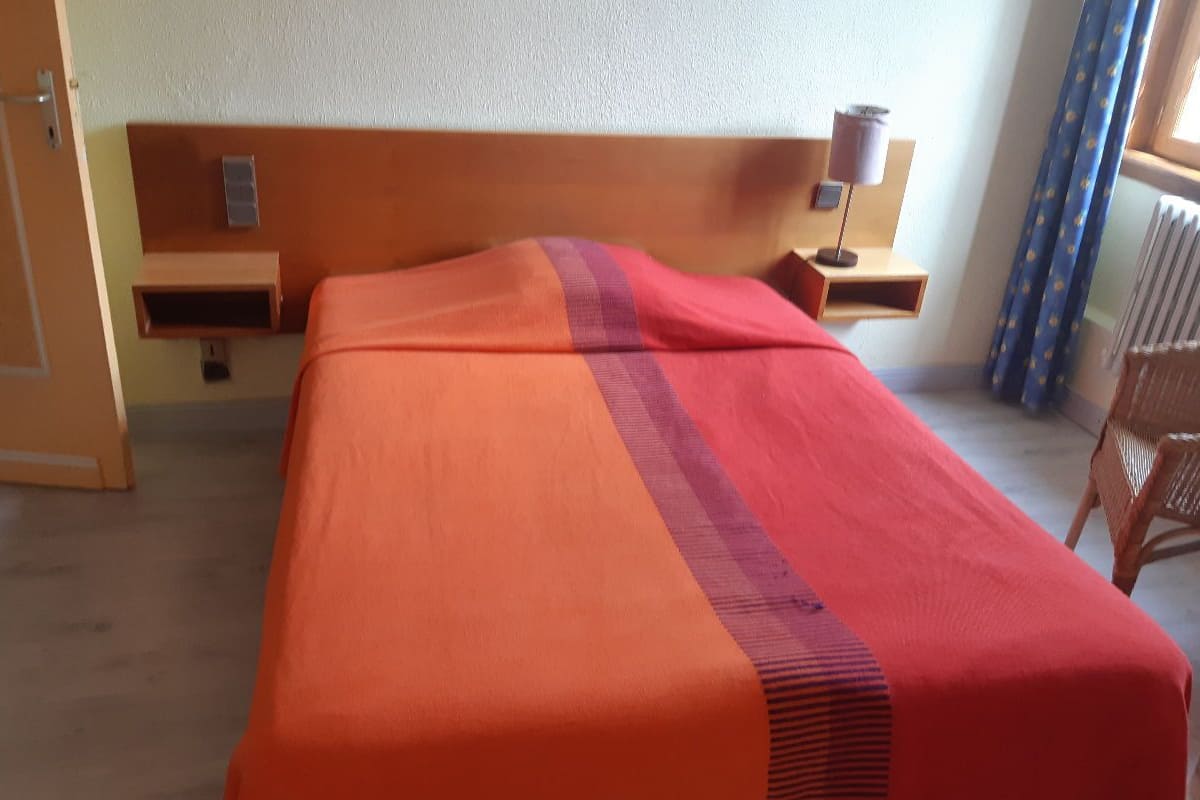 A hotel room with a bed, a nightstand, a lamp, a chair, and a window with curtains.