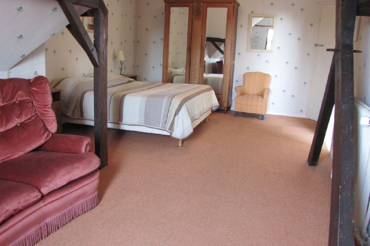 A bedroom with a bed, a red sofa, a wooden wardrobe, and a mirror.