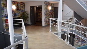 A multi-level interior with a staircase, wooden flooring, and walls decorated with colorful posters. - hotelF1 Cergy (Cergy)