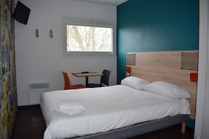 Habitación de hotel con cama, escritorio, silla, ventana y televisor fijado a la pared.