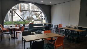 A modern cafe with a large arched window, multiple tables and chairs, and a view of the cityscape.