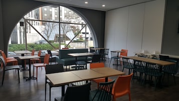 Un café moderno con un amplio ventanal en arco, varias mesas y sillas, y vistas a la ciudad.