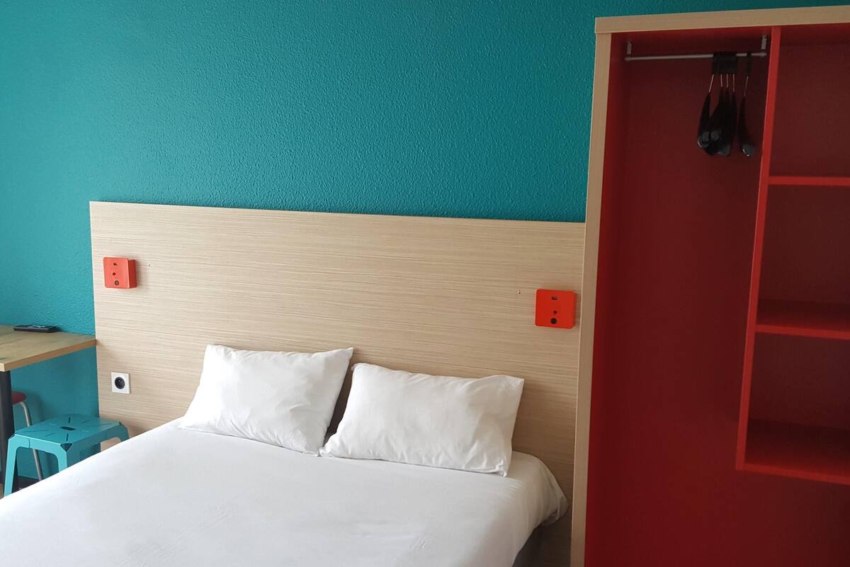 Una cama con ropa de cama blanca, un cabecero de madera y una pared color aguamarina.