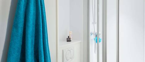 Un baño con cabina de ducha de vidrio, un perchero con una toalla azul y un pequeño estante con artículos de tocador.